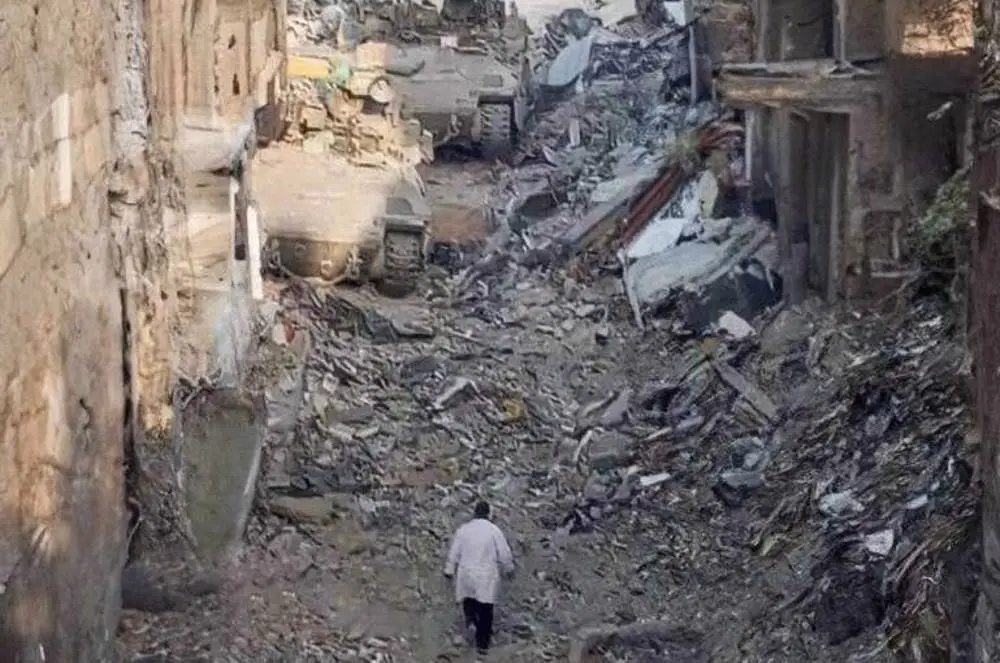 A person walks through rubble and destroyed buildings past a military vehicle in Gaza